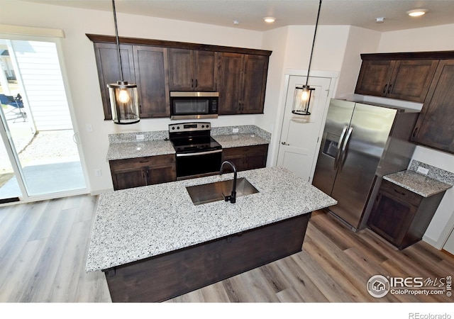 kitchen with stainless steel appliances, sink, pendant lighting, and light stone counters