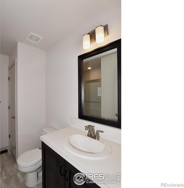 bathroom featuring vanity, a shower with shower door, and toilet