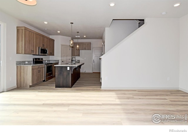 kitchen with light hardwood / wood-style floors, hanging light fixtures, appliances with stainless steel finishes, a kitchen island with sink, and sink