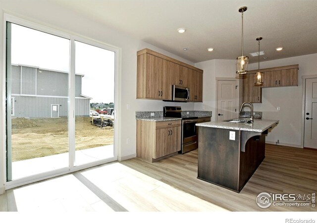 kitchen featuring light stone countertops, light wood-type flooring, appliances with stainless steel finishes, decorative light fixtures, and sink