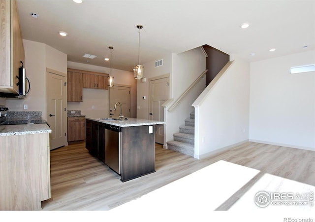 kitchen with light hardwood / wood-style floors, stainless steel dishwasher, a center island with sink, hanging light fixtures, and sink