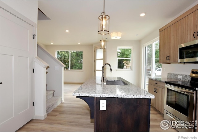 kitchen featuring light stone countertops, light hardwood / wood-style floors, a center island with sink, hanging light fixtures, and appliances with stainless steel finishes