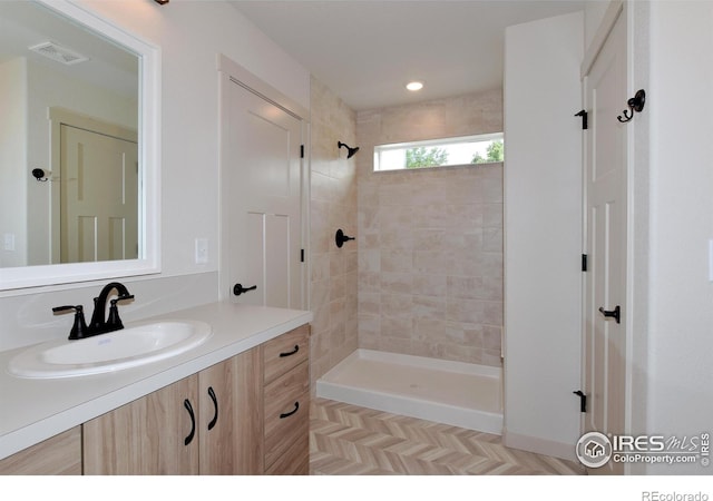 bathroom featuring tiled shower, parquet flooring, and vanity