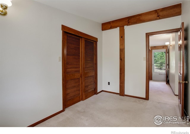 unfurnished bedroom featuring a closet, light colored carpet, and beam ceiling