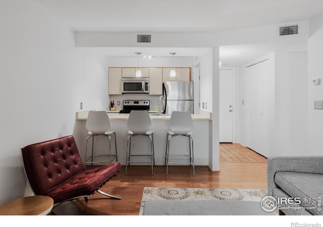 kitchen featuring pendant lighting, stainless steel appliances, light hardwood / wood-style floors, and cream cabinets