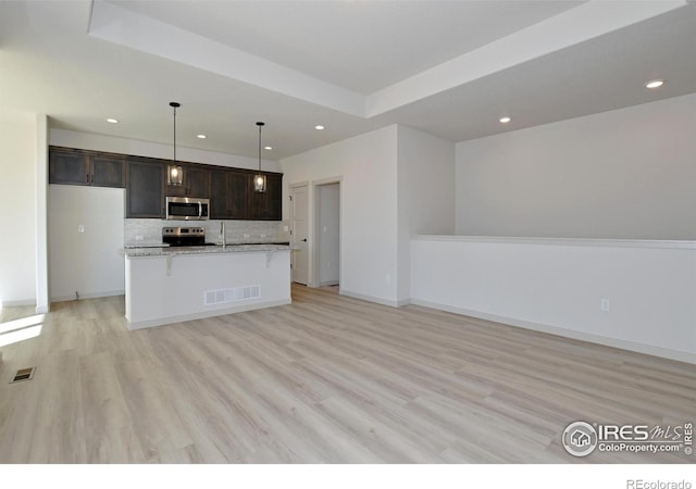 kitchen featuring hanging light fixtures, an island with sink, stainless steel appliances, dark brown cabinets, and light stone counters