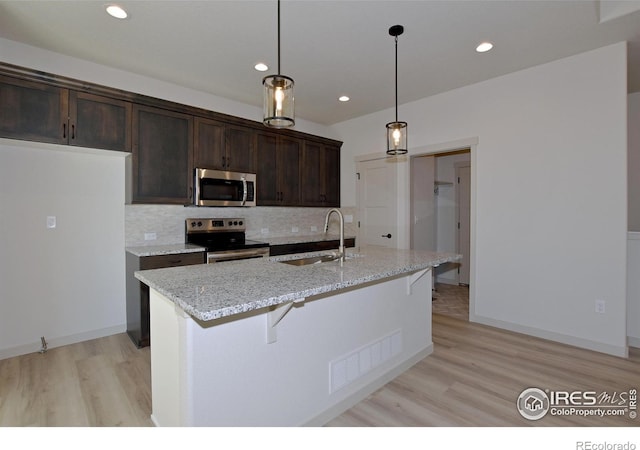 kitchen featuring stainless steel appliances, decorative backsplash, sink, hanging light fixtures, and light stone counters