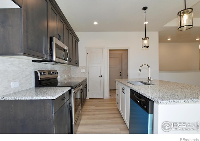 kitchen with light stone countertops, stainless steel appliances, sink, backsplash, and hanging light fixtures