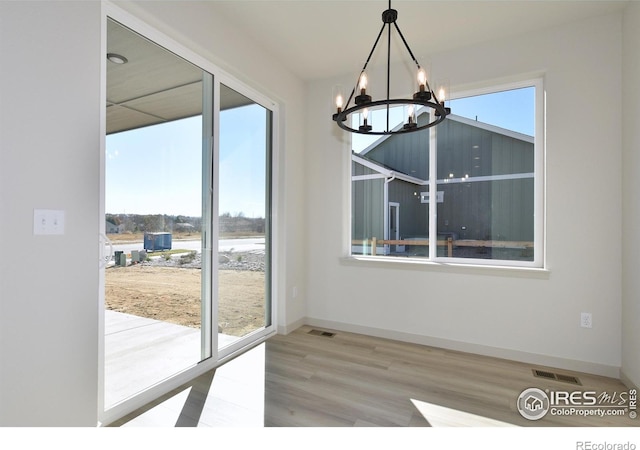 unfurnished dining area with light wood-type flooring, a chandelier, and plenty of natural light