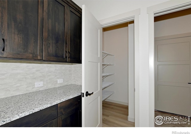 interior space with light wood-type flooring, decorative backsplash, dark brown cabinetry, and light stone countertops