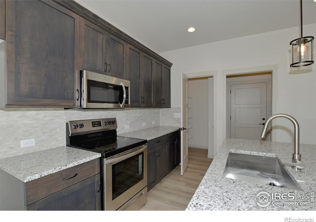 kitchen with stainless steel appliances, sink, decorative light fixtures, and light stone countertops