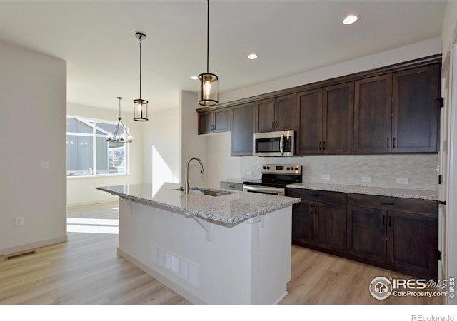 kitchen featuring pendant lighting, sink, a kitchen island with sink, light stone countertops, and stainless steel appliances