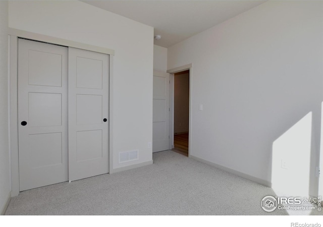 unfurnished bedroom with light colored carpet and a closet