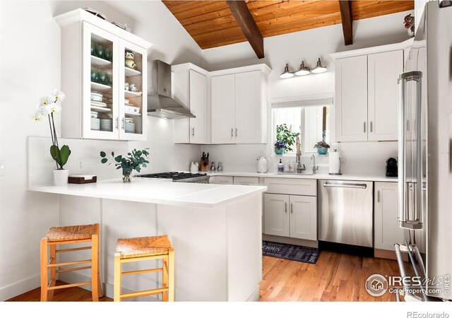 kitchen with wall chimney exhaust hood, wooden ceiling, stainless steel appliances, vaulted ceiling with beams, and white cabinetry