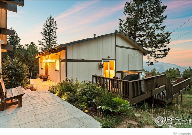 back house at dusk with a deck with mountain view and a patio