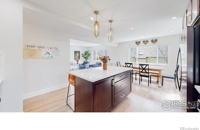 kitchen featuring pendant lighting, a center island, stainless steel fridge, light hardwood / wood-style floors, and a kitchen bar