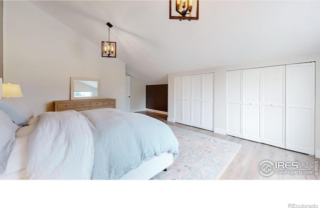 bedroom with a chandelier, two closets, lofted ceiling, and light hardwood / wood-style flooring