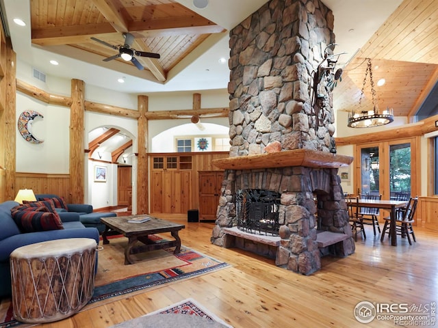living room featuring ceiling fan with notable chandelier, hardwood / wood-style floors, wood ceiling, a stone fireplace, and wooden walls