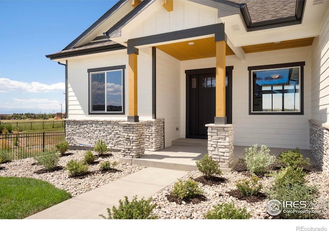 entrance to property featuring stone siding, fence, covered porch, and board and batten siding