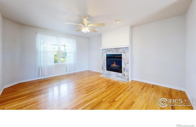 unfurnished living room featuring ceiling fan, a tile fireplace, and light hardwood / wood-style flooring