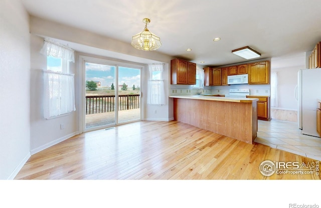 kitchen featuring kitchen peninsula, light wood-type flooring, white appliances, decorative light fixtures, and a chandelier