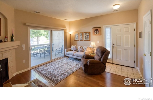 living room with light wood-type flooring and a tiled fireplace