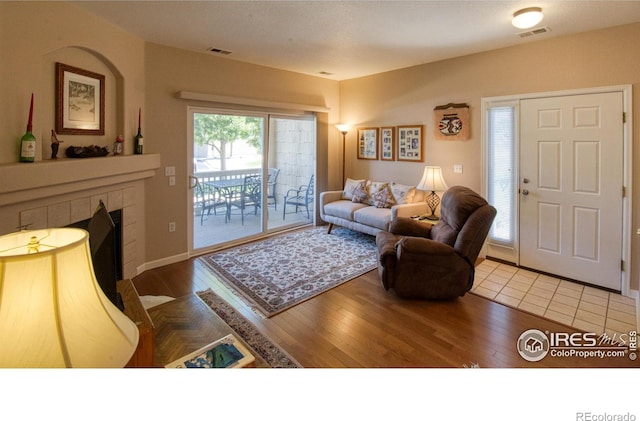 living room with wood-type flooring and a tiled fireplace