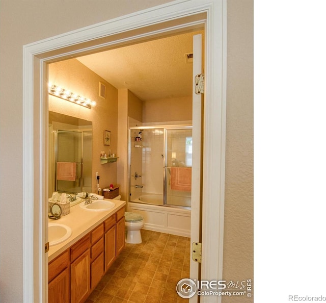 full bathroom featuring combined bath / shower with glass door, a textured ceiling, vanity, and toilet