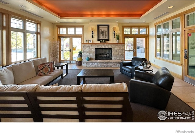 tiled living room featuring french doors, a raised ceiling, and a fireplace