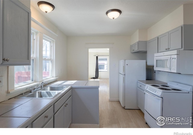 kitchen with light hardwood / wood-style floors, gray cabinets, white appliances, and sink