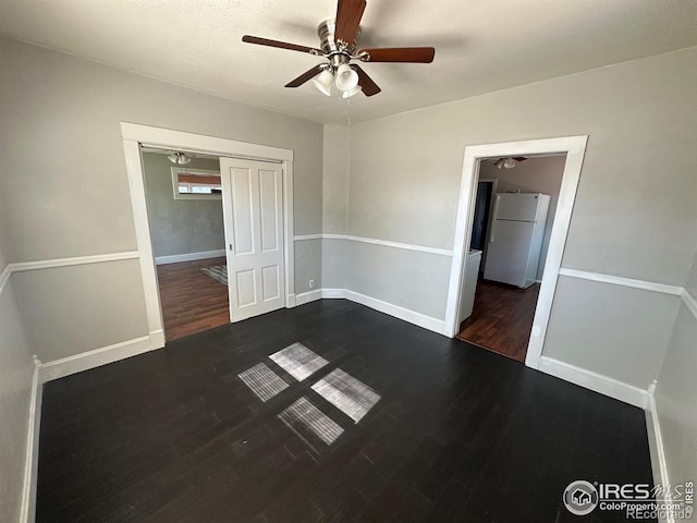 unfurnished bedroom with ceiling fan, a closet, white fridge, and dark hardwood / wood-style floors