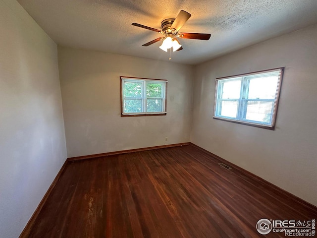 empty room with a textured ceiling, ceiling fan, and dark hardwood / wood-style floors