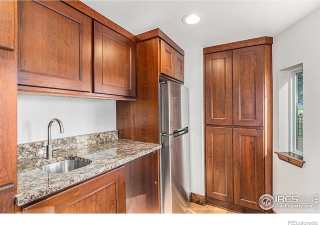 kitchen with stainless steel fridge, light stone counters, and sink