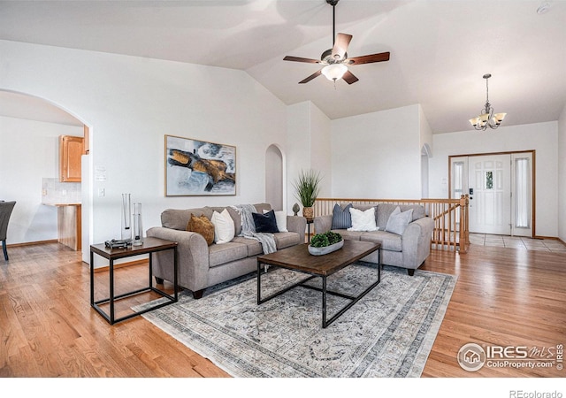 living room featuring ceiling fan with notable chandelier, lofted ceiling, and light wood-type flooring