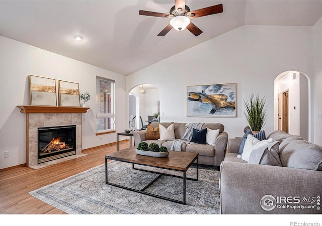 living room with a tiled fireplace, ceiling fan, light hardwood / wood-style flooring, and vaulted ceiling