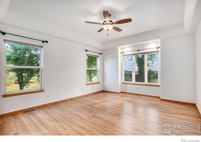 unfurnished room with ceiling fan, light wood-type flooring, a wealth of natural light, and a tray ceiling