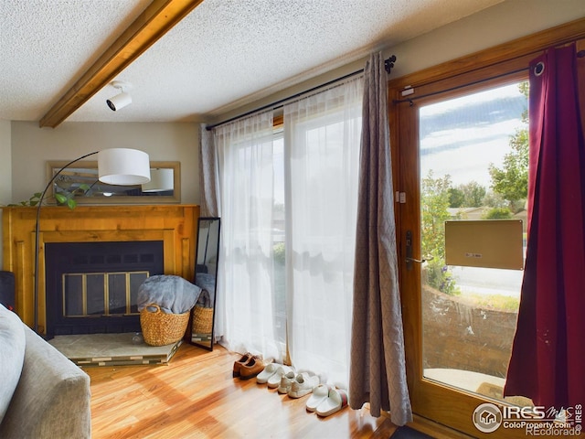 bedroom featuring a textured ceiling, beam ceiling, wood finished floors, and a glass covered fireplace