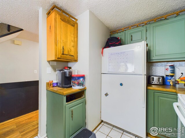 kitchen featuring stove, decorative backsplash, light wood-type flooring, a textured ceiling, and white fridge