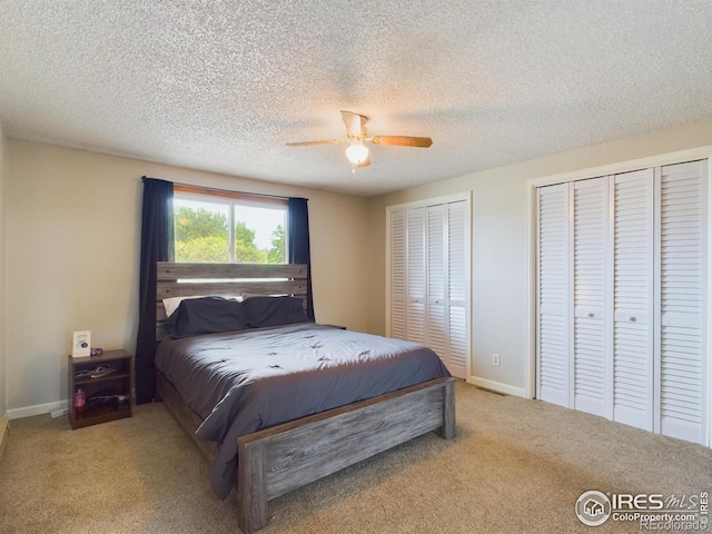 carpeted bedroom featuring baseboards, a textured ceiling, a ceiling fan, and multiple closets