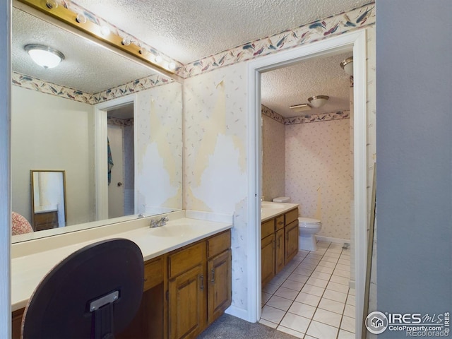 full bathroom with wallpapered walls, toilet, two vanities, a textured ceiling, and a sink