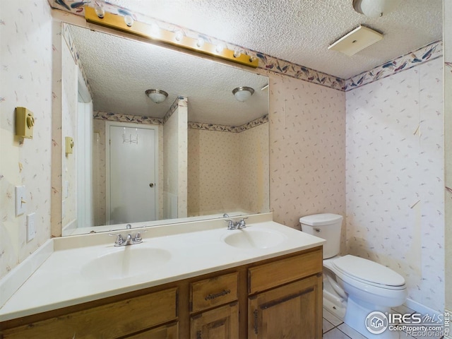 bathroom with toilet, a textured ceiling, tile patterned flooring, and dual bowl vanity