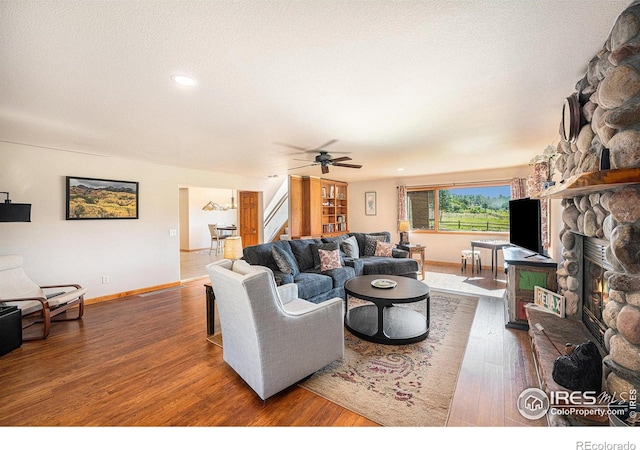 living room featuring a stone fireplace, dark wood-type flooring, and ceiling fan