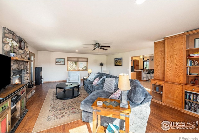 living room with ceiling fan, a stone fireplace, and hardwood / wood-style floors