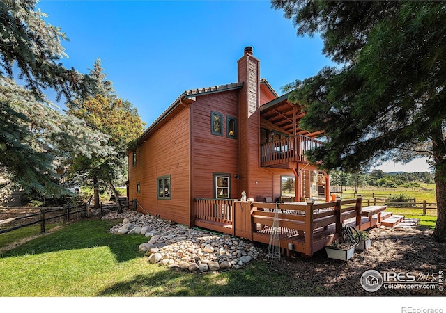 rear view of house with a wooden deck, a balcony, a yard, and a rural view