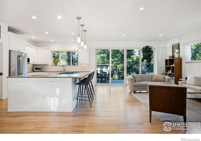 kitchen featuring white cabinetry, high end refrigerator, backsplash, pendant lighting, and a kitchen bar