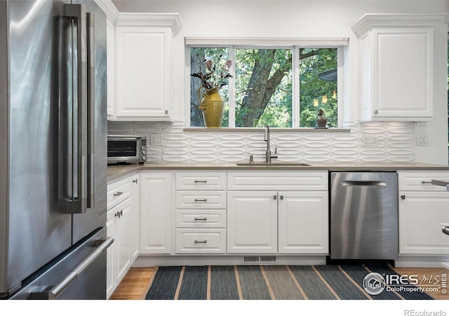 kitchen featuring tasteful backsplash, stainless steel refrigerator, white cabinetry, and sink