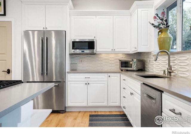 kitchen featuring sink, backsplash, light hardwood / wood-style floors, white cabinets, and appliances with stainless steel finishes