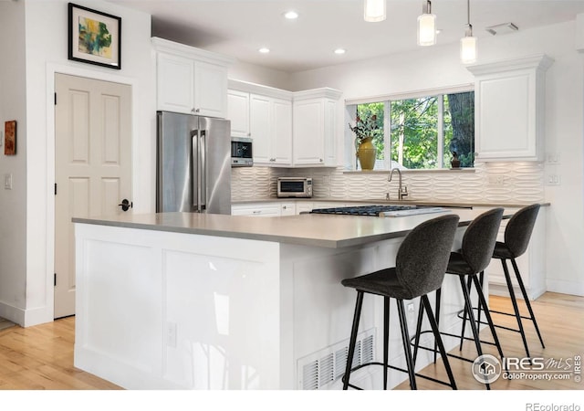 kitchen with white cabinets, appliances with stainless steel finishes, a kitchen island, and hanging light fixtures