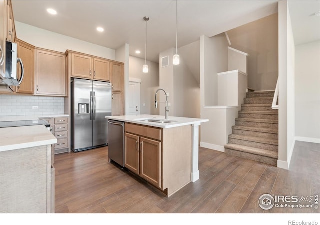 kitchen with sink, appliances with stainless steel finishes, hardwood / wood-style flooring, decorative backsplash, and a kitchen island with sink