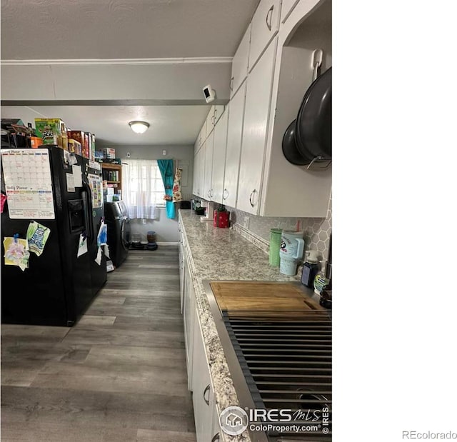 kitchen featuring washer / clothes dryer, white cabinets, black refrigerator with ice dispenser, and wood finished floors